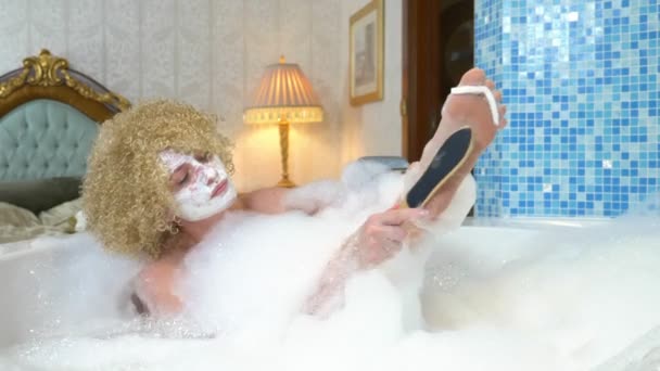 Cheerful blonde woman does pedicure while taking a bath with foam — Stock Video