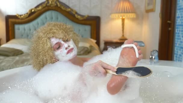 Femme blonde gaie fait pédicure tout en prenant un bain avec de la mousse — Video