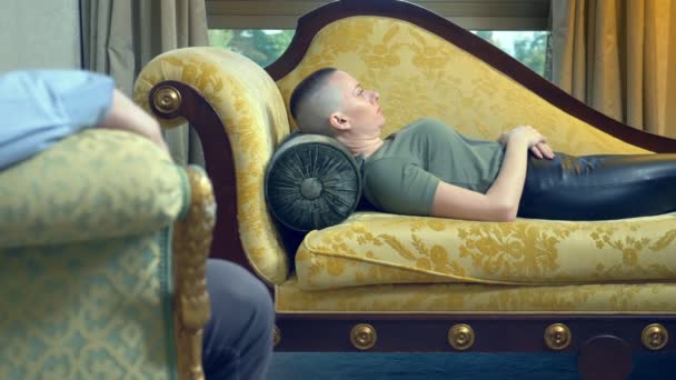 Ψυχολόγος δουλεύει με μια νεαρή φαλακρή γυναίκα ξαπλωμένη σε έναν καναπέ σε ένα κομψό γραφείο — Αρχείο Βίντεο