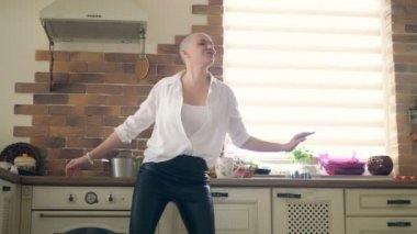 Orta boy. Genç, inanılmaz duygusal, kel kadın evdeki mutfakta dans ediyor.