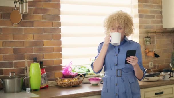 Середній постріл. стильна жінка використовує мобільний телефон на кухні вдома — стокове відео