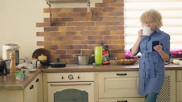 Un tiro medio. mujer elegante usando un teléfono móvil en la cocina en casa — Foto de Stock