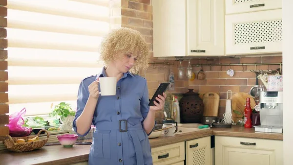 Un tiro medio. mujer elegante usando un teléfono móvil en la cocina en casa — Foto de Stock