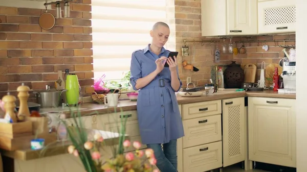 Un tiro medio. mujer calva con estilo utilizando el teléfono celular en la cocina en casa — Foto de Stock
