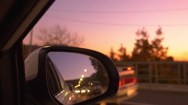 View from the car window to the rear view mirror. Traffic jam in the evening, against the backdrop of a beautiful lilac sunset sky — Stock Photo, Image