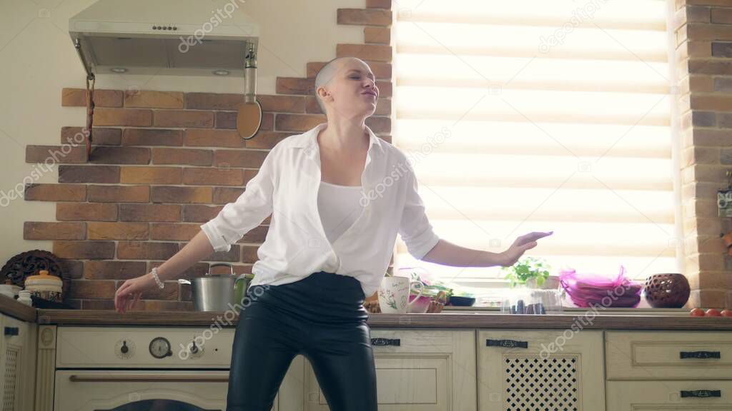 medium shot. young amazingly emotional bald woman dancing in the kitchen at home