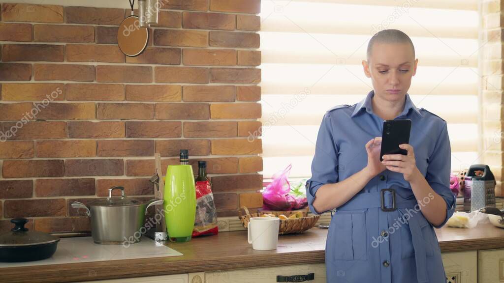 medium shot. stylish bald woman using cellphone in kitchen at home