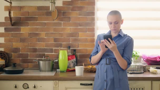 Medium shot. stylish bald woman using cellphone in kitchen at home — Stock Video