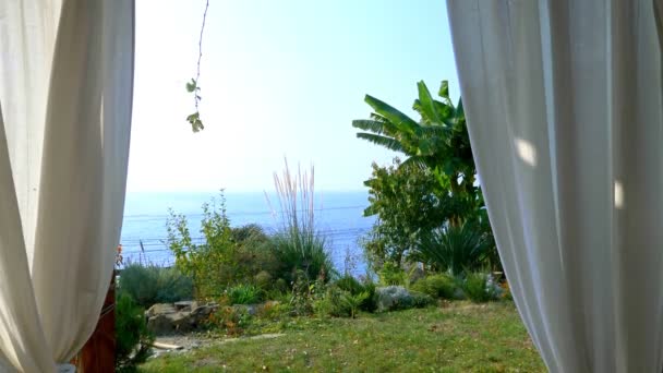 Cortinas blancas en el cenador. mar, horizonte y plantas verdes — Vídeos de Stock