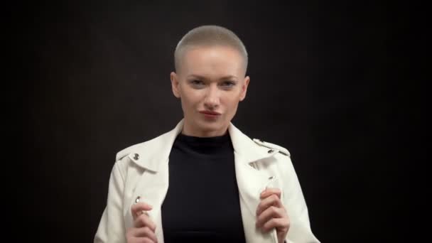 Blond woman with short hair on a black background in a white leather jacket. — Stock Video