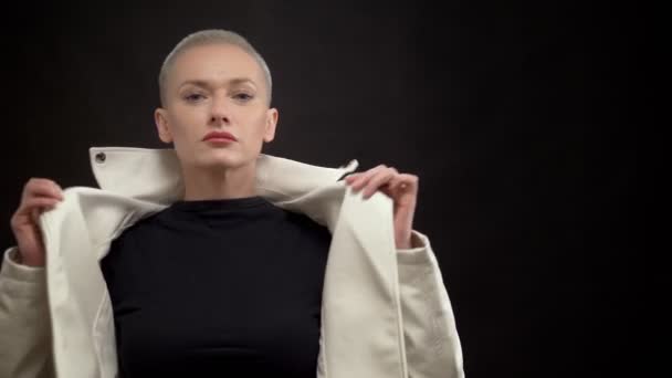Blonde Frau mit kurzen Haaren auf schwarzem Hintergrund in weißer Lederjacke. — Stockvideo