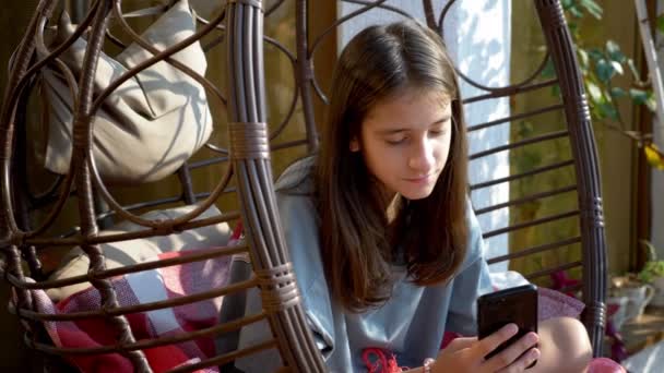 Милая девочка-подросток отдыхает в качелях на заднем дворе, используя смартфон — стоковое видео