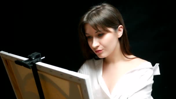 Krásná brunetka dívka umělec maluje obrázek na plátno. černé pozadí — Stock video