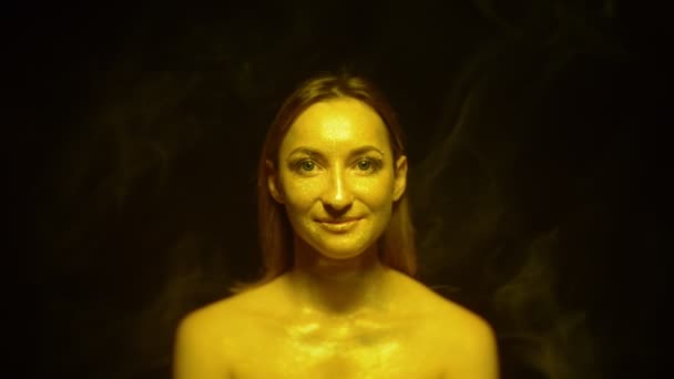 Vrouwelijk gezicht met glitter op een zwarte achtergrond met gekleurde rook — Stockvideo