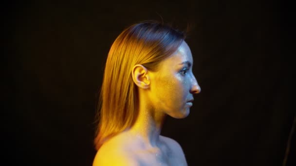 Frau mit Funkeln im Gesicht in farbigem Licht auf schwarzem Hintergrund — Stockvideo