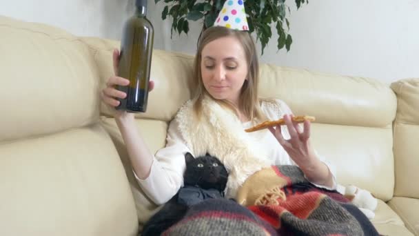 Samotna dziewczyna w imprezowym kapeluszu, pijąca wino z butelki z kotem — Wideo stockowe