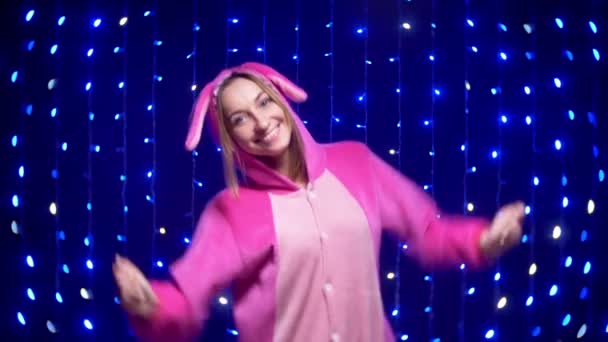 Cheerful girl in pink pajamas kigurumi dancing on the background of garlands — Stock Video