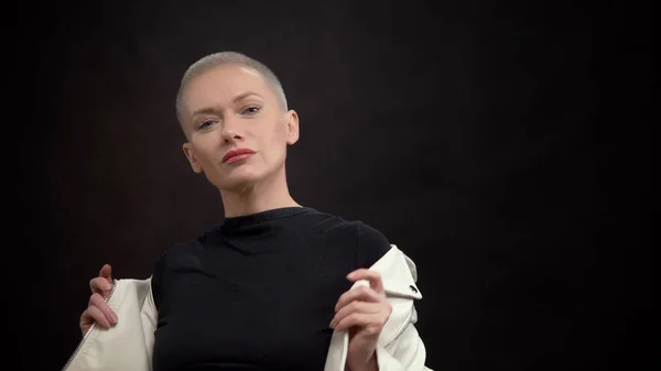 Mujer elegante con el pelo corto sobre un fondo negro en una chaqueta de cuero blanco —  Fotos de Stock