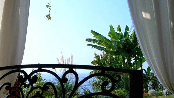 Bílé záclony v altánku. moře, horizont a zelené rostliny. — Stock fotografie