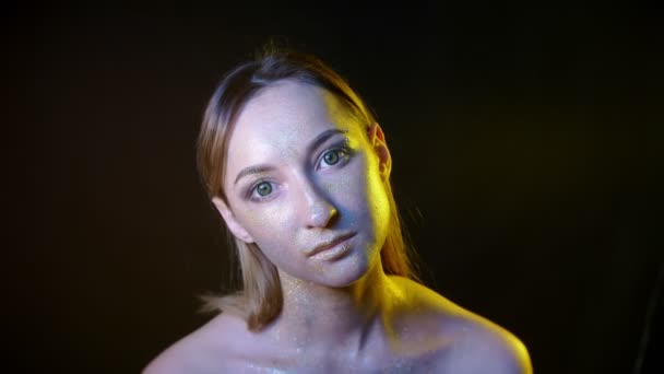 Žena s jiskry na tváři v barevném světle na černém pozadí — Stock video