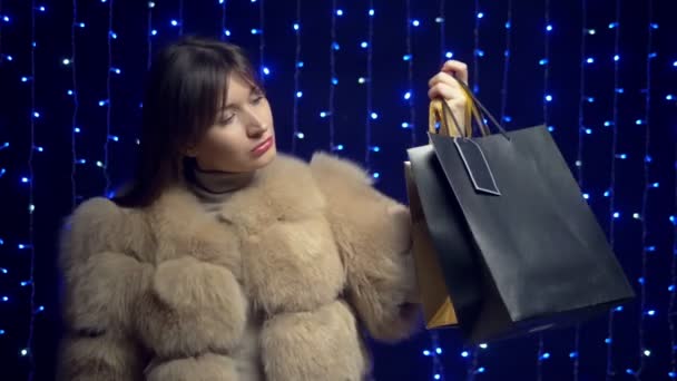Stylish girl in a fur coat with packages on a background garlands. shopping sale — ストック動画