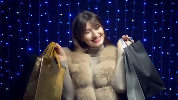 Stylish girl in a fur coat with packages on a background garlands. shopping sale — Stock Video