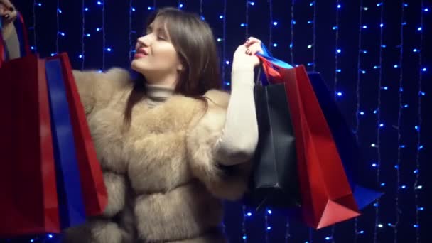 Stylish girl in a fur coat with packages on a background garlands. shopping sale — 图库视频影像