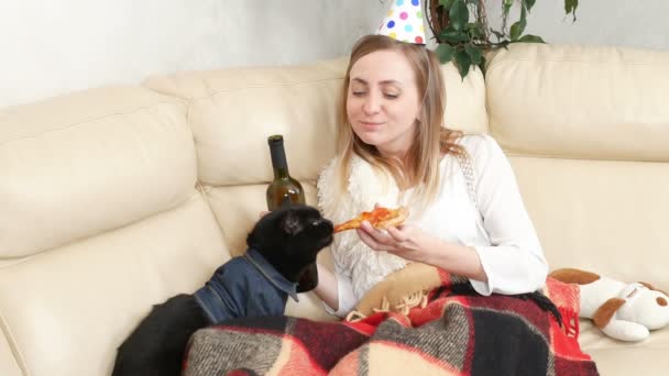 Egy magányos lány egy party kalapban, bort iszik az üvegből egy macskával. — Stock videók