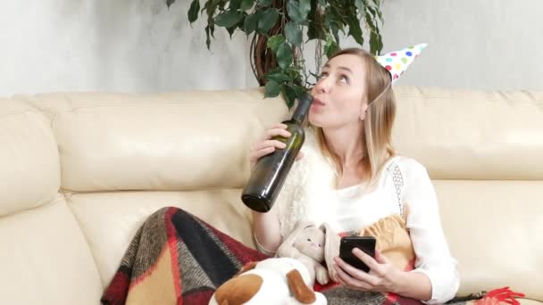 Egy magányos lány, hogy egyedül ünnepeljen egy üveg borral otthon, mobiltelefonnal. — Stock videók