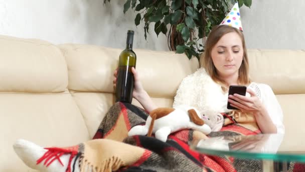 Egy magányos lány, hogy egyedül ünnepeljen egy üveg borral otthon, mobiltelefonnal. — Stock videók