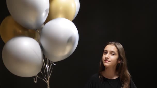 Bonito menina segurando balões ouro e prata cores em um fundo preto — Vídeo de Stock