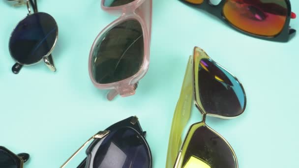 青い背景の上にランダムに横たわるサングラスのセット。ファッションデザイン — ストック動画