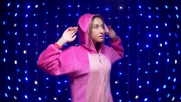 Menina alegre em pijama rosa kigurumi dançando no fundo de guirlandas — Vídeo de Stock