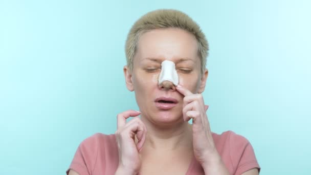 Жінка з пов'язкою після ринопластики подряпає їй ніс під відливом — стокове відео