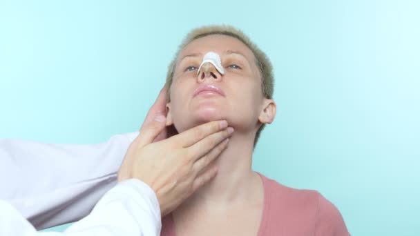 Las manos del médico tocan la cara de una mujer con un vendaje en la nariz . — Vídeo de stock