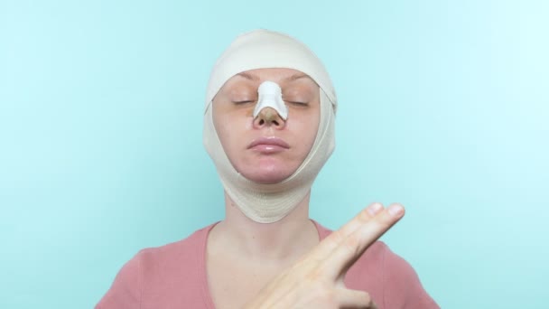 Las manos del médico tocan la cara de una mujer con un vendaje en la nariz y la cara — Vídeos de Stock