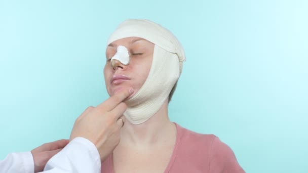 As mãos do médico tocam o rosto de uma mulher com uma bandagem no nariz e no rosto — Vídeo de Stock