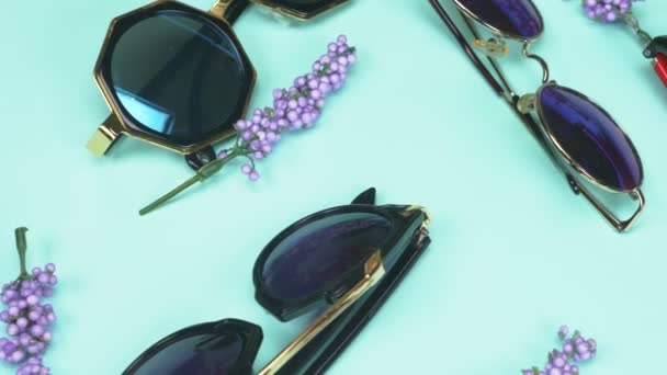 En uppsättning solglasögon slumpmässigt liggande på en blå bakgrund. modedesign — Stockvideo