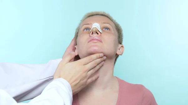 Las manos del médico tocan la cara de una mujer con un vendaje en la nariz . — Foto de Stock