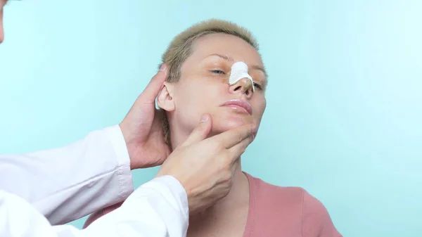 As mãos do médico toca o rosto de uma mulher com uma bandagem no nariz . — Fotografia de Stock