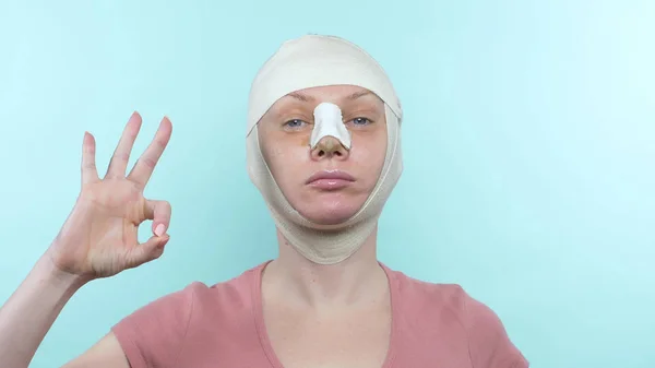 Kobieta po operacji plastycznej z bandażem na twarzy i nosie. pokazuje super znak — Zdjęcie stockowe