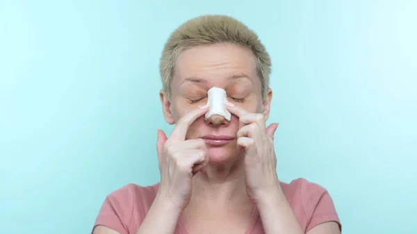 Een vrouw met een verband na neuscorrectie krabt haar neus onder een gips — Stockfoto