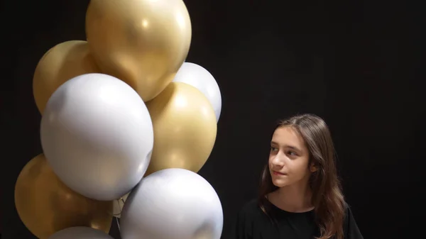 在黑色背景上拿着金色和银色气球的可爱女孩 — 图库照片