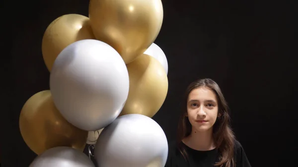 Fată drăguță care deține baloane de aur și culori argintii pe un fundal negru — Fotografie, imagine de stoc
