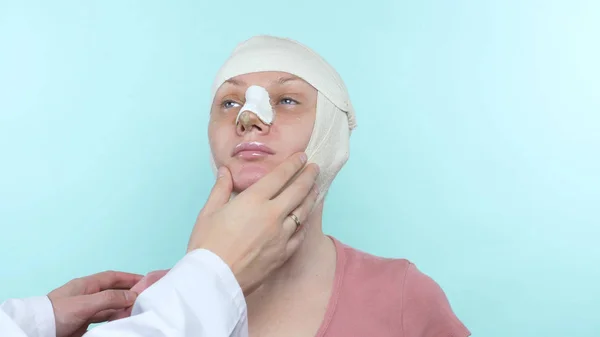 Las manos del médico tocan la cara de una mujer con un vendaje en la nariz y la cara — Foto de Stock