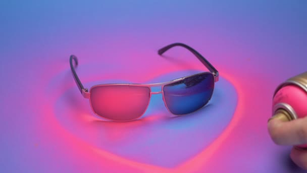Óculos de sol são pintados de rosa com tinta spray em um fundo azul — Vídeo de Stock