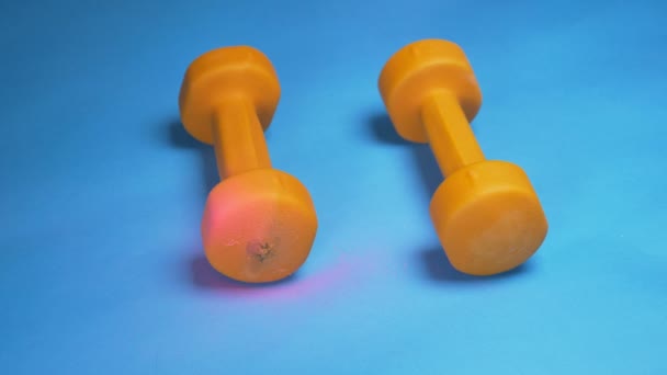 O processo de colorir halteres laranja com tinta spray rosa. fundo azul — Vídeo de Stock