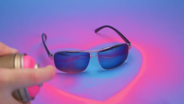 Sonnenbrille ist rosa lackiert mit Sprühfarbe auf blauem Hintergrund — Stockvideo