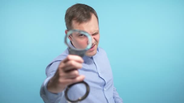 A man looks into the camera and shows the handcuffs. blue background — Stock Video