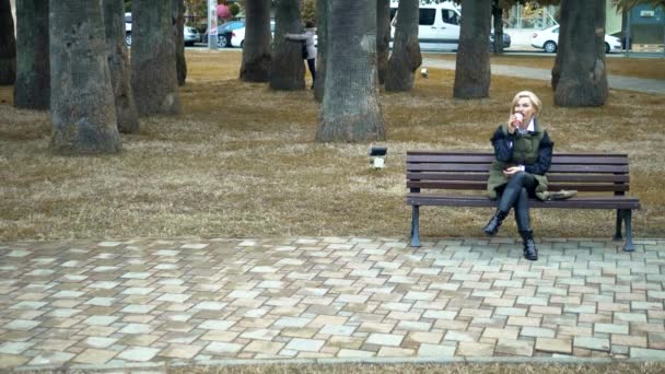 Stijlvolle blonde vrouw zittend op de bank in het najaar Park — Stockvideo